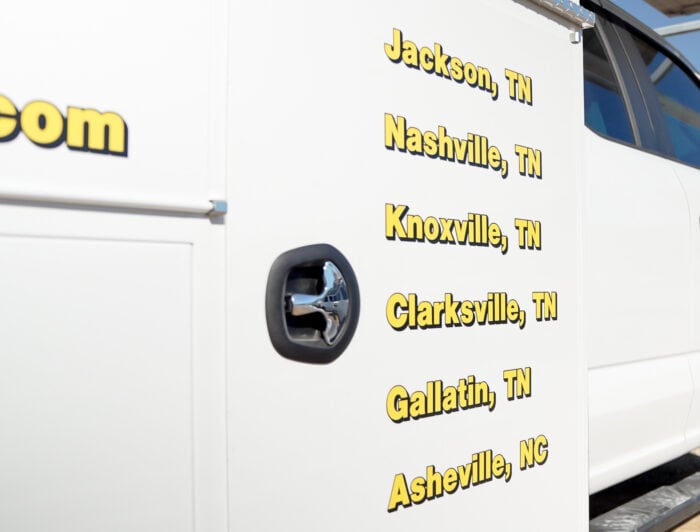 Side view of a white vehicle with yellow text listing locations: Jackson, Nashville, Knoxville, Clarksville, Gallatin (TN), and Asheville (NC).