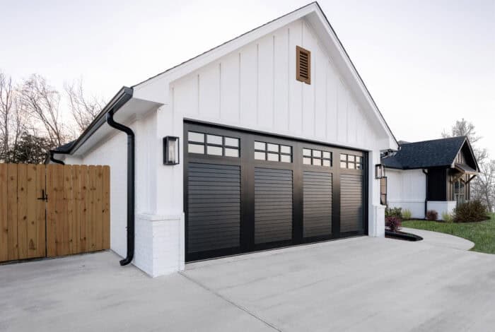 A modern white house with a black two-car garage, a fenced yard, and an attached sloped roof.