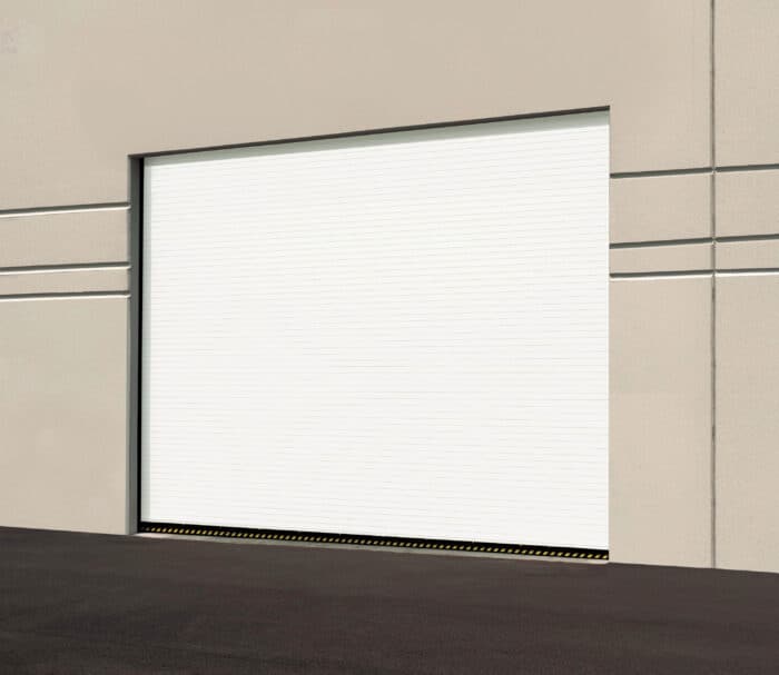 A sturdy white industrial garage door on a beige building, highlighted by a black-and-yellow caution strip at the base. Perfect for anyone looking into garage door replacement options.