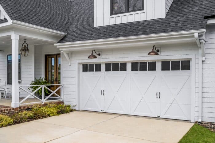 White garage with carriage-style doors and driveway, attached to a house with a covered porch and decorative lighting.